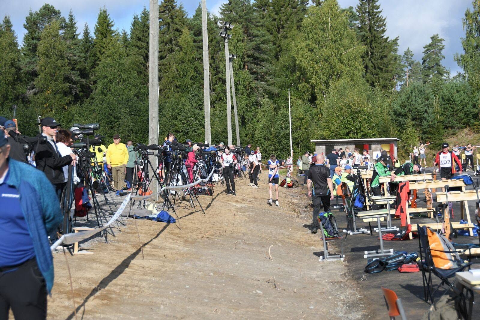 Spectators with spotting scopes along a summer biathlon shooting range