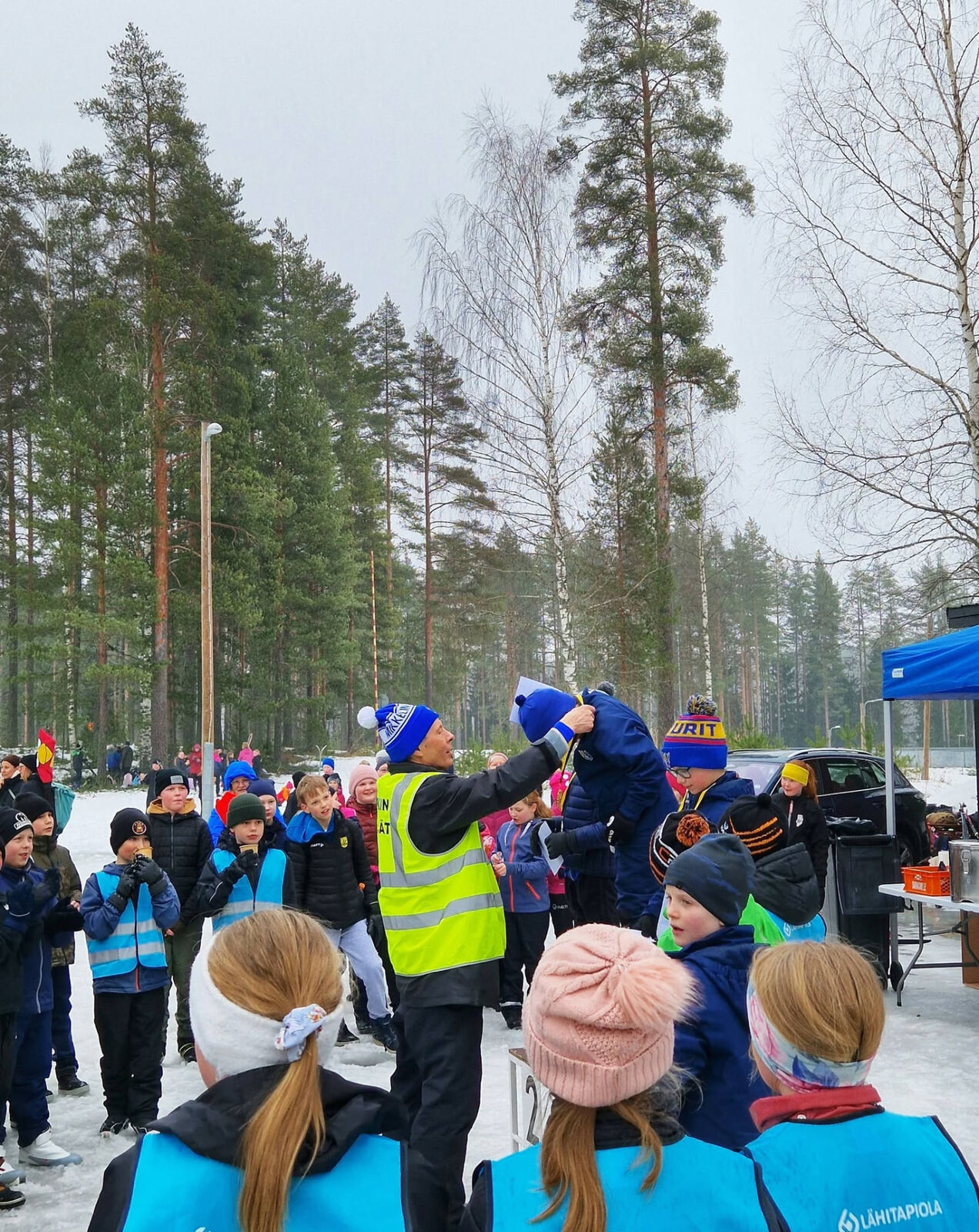 A volunteer in a high-visibility vest awarding a medal to a child in the snow